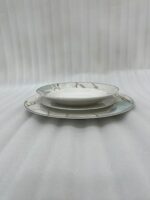 A neatly stacked 18-piece super bone china dinner plate set featuring a white and mint green marble pattern with gold veining, arranged on a dining table with silverware and a crystal glass.