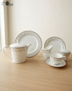 A complete 24-piece luxury tea set on a wooden table, featuring a white porcelain teapot, milk jug, sugar pot, cups, saucers, and plates with delicate silver fern patterns.