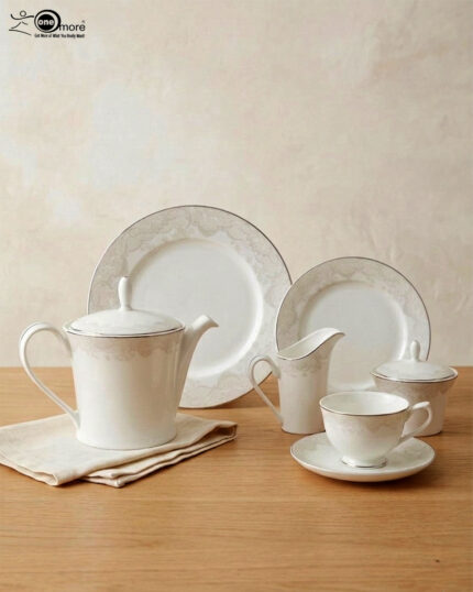 A complete 24-piece white porcelain tea set featuring delicate lace-patterned edges and silver trim, arranged on a wooden table.