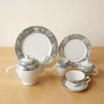 A 24-piece porcelain tea set featuring a modern grey marble pattern border with silver accents, including a teapot, milk pot, sugar bowl, cups, saucers, and plates arranged on a wooden surface.