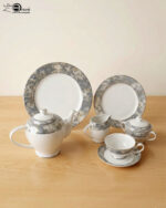 A 24-piece porcelain tea set featuring a modern grey marble pattern border with silver accents, including a teapot, milk pot, sugar bowl, cups, saucers, and plates arranged on a wooden surface.