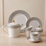A 24-piece luxury porcelain tea set featuring a crisp white finish, sophisticated grey floral patterned rims, and delicate gold accents, arranged on a glossy surface.