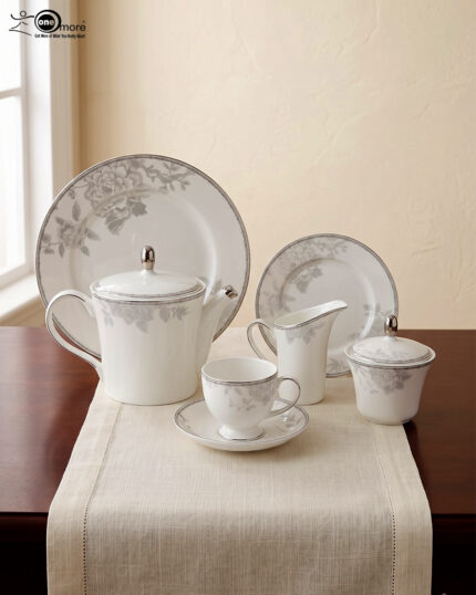 A sophisticated 24-piece white porcelain tea set featuring a delicate grey floral pattern and silver trim, arranged elegantly on a table runner.