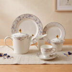 A 24-piece luxury porcelain tea set featuring a delicate blue floral pattern, gold accents, and striped borders, arranged elegantly on a linen runner.