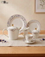 A 24-piece luxury porcelain tea set featuring a delicate blue floral pattern, gold accents, and striped borders, arranged elegantly on a linen runner.