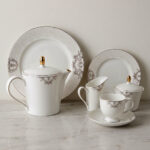 A complete 24-piece porcelain tea set featuring a teapot, sugar bowl, milk jug, tea cups, saucers, and plates, all decorated with intricate grey filigree patterns and gold accents, displayed on a marble surface.