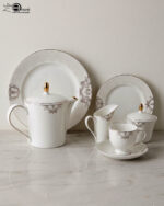A complete 24-piece porcelain tea set featuring a teapot, sugar bowl, milk jug, tea cups, saucers, and plates, all decorated with intricate grey filigree patterns and gold accents, displayed on a marble surface.