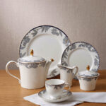 A 24-piece luxury porcelain tea set featuring a delicate blue floral pattern with gold trim, including a teapot, cups, saucers, plates, and serving accessories on a wooden table.