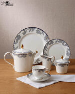 A 24-piece luxury porcelain tea set featuring a delicate blue floral pattern with gold trim, including a teapot, cups, saucers, plates, and serving accessories on a wooden table.