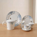 A complete 24-piece luxury porcelain tea set featuring a delicate blue floral pattern on white china with silver rims, displayed on a wooden table.