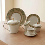 A 24-piece luxury porcelain tea set featuring white ceramic with a soft green brushstroke border and gold-tone accents, arranged on a light wooden table.