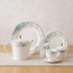 A 24-piece luxury porcelain tea set featuring a white base, marble-patterned rims in blue and grey, and delicate gold detailing, arranged on a wooden table.
