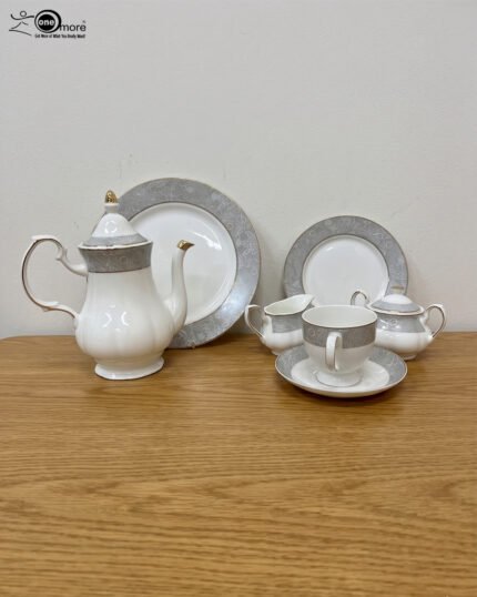 : A complete 24-piece white porcelain tea set featuring delicate grey floral patterns with gold trim, including a teapot, teacups, saucers, and plates, arranged on a wooden surface.