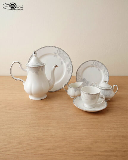 A 24-piece white porcelain tea set featuring delicate gray floral patterns and silver trim, arranged on a light wooden surface.
