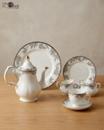 A 24-piece luxury porcelain tea set featuring a white teapot, milk jug, sugar pot, cups, saucers, and plates adorned with delicate gray floral patterns and gold rims on a wooden table.