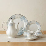 A 24-piece luxury porcelain tea set featuring a delicate blue floral pattern and silver trim, including a teapot, cups, saucers, plates, sugar bowl, and milk jug on a linen runner.