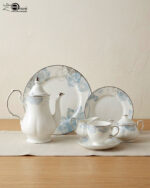 A 24-piece luxury porcelain tea set featuring a delicate blue floral pattern and silver trim, including a teapot, cups, saucers, plates, sugar bowl, and milk jug on a linen runner.