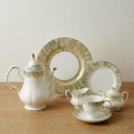 A 24-piece luxury porcelain tea set featuring white dishes with soft green, brush-stroke patterned edges and delicate gold rims, displayed on a wooden surface.