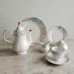 A luxurious 24-piece porcelain tea set featuring white ceramic with blue marble patterns and gold trim, displayed on a marble surface.