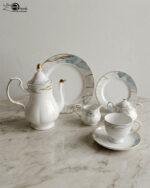 A luxurious 24-piece porcelain tea set featuring white ceramic with blue marble patterns and gold trim, displayed on a marble surface.