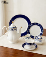 A 24-piece luxury porcelain tea set featuring a classic blue and white floral pattern with gold trim, including a teapot, cups, saucers, and plates, arranged on a beige table runner.