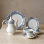 A 24-piece luxury porcelain tea set featuring a white base with elegant blue marble-patterned rims and gold accents, displayed on a textured stone surface including a teapot, cups, saucers, plates, sugar pot, and creamer.