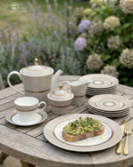 A premium Super Bone China tea set featuring a teapot, sugar bowl, creamer, and cups and saucers with a tan pinstripe pattern and gold-rimmed borders, arranged on a wooden table outdoors with avocado toast on a plate.