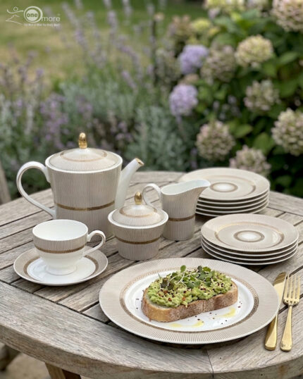 A premium Super Bone China tea set featuring a teapot, sugar bowl, creamer, and cups and saucers with a tan pinstripe pattern and gold-rimmed borders, arranged on a wooden table outdoors with avocado toast on a plate.
