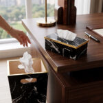 A matching executive desk accessory set featuring a black marble pattern wastebasket and a rectangular tissue box cover with elegant gold trim, placed on a dark wooden office desk.