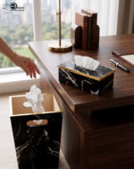A matching executive desk accessory set featuring a black marble pattern wastebasket and a rectangular tissue box cover with elegant gold trim, placed on a dark wooden office desk.