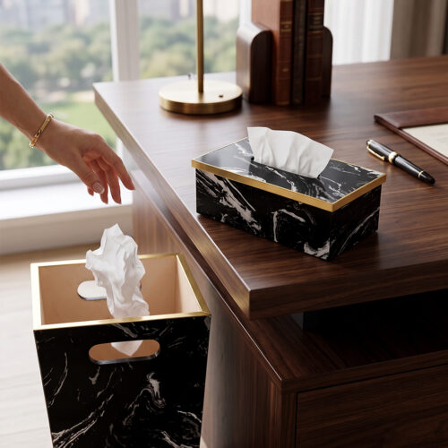 A matching executive desk accessory set featuring a black marble pattern wastebasket and a rectangular tissue box cover with elegant gold trim, placed on a dark wooden office desk.
