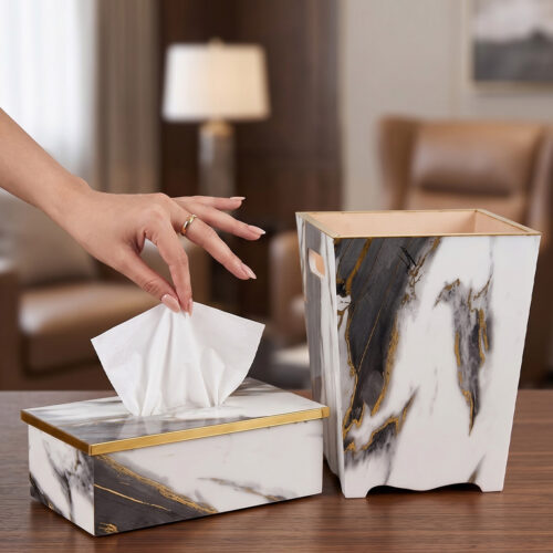 A luxury white and black marble-patterned tissue box holder and matching wastebasket with elegant gold trim, displayed on a wooden table.