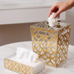 Clear acrylic dustbin and matching tissue box holder with a gold geometric lattice pattern on a white marble tabletop.