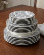 A stacked 18-piece super bone china dinnerware set featuring a grey and white floral pattern on a wooden table, including rice, deep, and quarter plates.