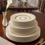 A stacked 18-piece super bone china plate set with a gold sunburst design on a wooden dining table.