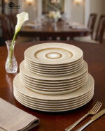 A stacked 18-piece super bone china plate set with a gold sunburst design on a wooden dining table.