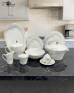 An elegant 61-piece white Super Bone China dinner set with blue feather patterns and gold accents, displayed on a black marble countertop in a kitchen