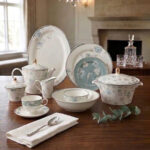 A luxury 61-piece Super Bone China dinner set with blue floral patterns and silver rims displayed on a wooden dining table, including plates, bowls, a teapot, and a serving casserole.
