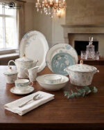 A luxury 61-piece Super Bone China dinner set with blue floral patterns and silver rims displayed on a wooden dining table, including plates, bowls, a teapot, and a serving casserole.