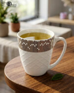 A steaming cup of green tea in a white bone china mug with a bronze geometric pattern and embossed lattice texture, sitting on a wooden table
