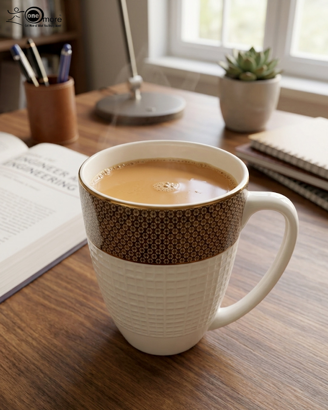 3 A high-angle close-up of a premium bone tea mug filled with hot tea, featuring a gold-rimmed floral pattern and a white textured base on a wooden desk with a book and succulent in the background