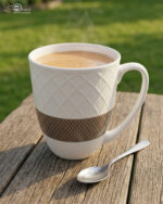 A set of six premium white ceramic tea mugs with a textured lattice design and a brown patterned base, filled with steaming tea and placed on a wooden outdoor table next to a silver spoon