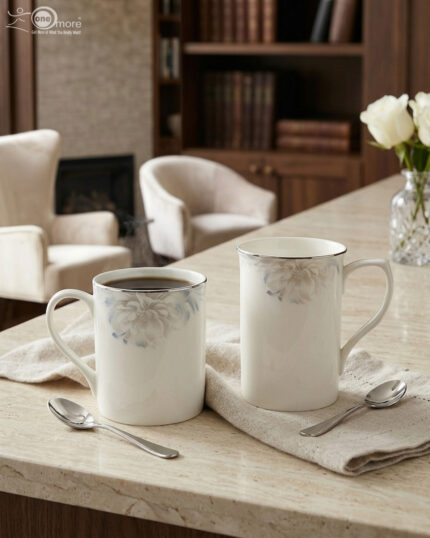 A high-angle shot labeled 3.jpg showing two elegant white bone china mugs with floral patterns and silver rims on a marble countertop next to silver spoons