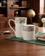 Set of two white bone china mugs from 3.jpg on a wooden table with a green placemat; one tall mug and one short mug, both featuring a grey marble pattern band and silver trim against a library background with cinematic lighting