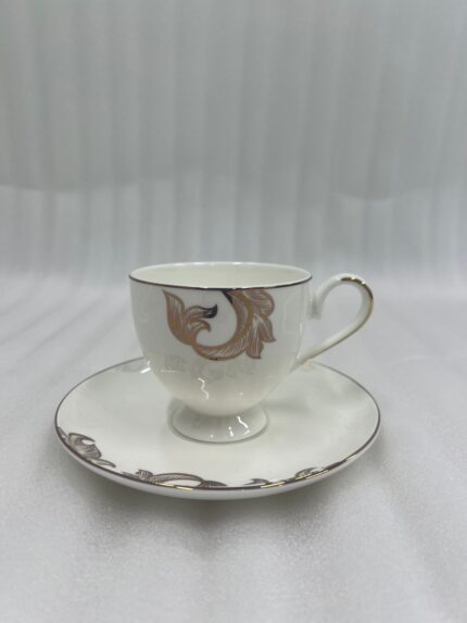 A steaming stream of milk tea being poured into a luxury white Super Bone China cup with gold-leaf designs, resting on a matching saucer with a silver spoon on a dark wooden table