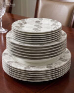 A complete Super Bone China dinner set from 6.jpg, featuring a white base with intricate grey floral borders. The set includes plates, bowls, a teapot, a tureen, and teacups displayed on a wooden surface.