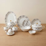 A complete white Super Bone dinner set featuring grey floral patterns and gold accents, including plates, bowls, a teapot, and serving dishes, displayed on a wooden surface in 3.jpg.
