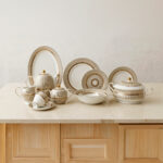 A luxury Super Bone China dinnerware set featuring a white porcelain base with intricate gold vertical ribbing and circular patterns, displayed on a marble countertop in 3.jpg