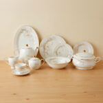 Luxury Super Bone China dinnerware set featuring a delicate white floral pattern, gold-rimmed edges, and matching tea service pieces on a wooden surface