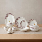 A luxury super bone china dinnerware set featuring a white base with intricate purple leaf patterns and gold accents, displayed on a wooden table